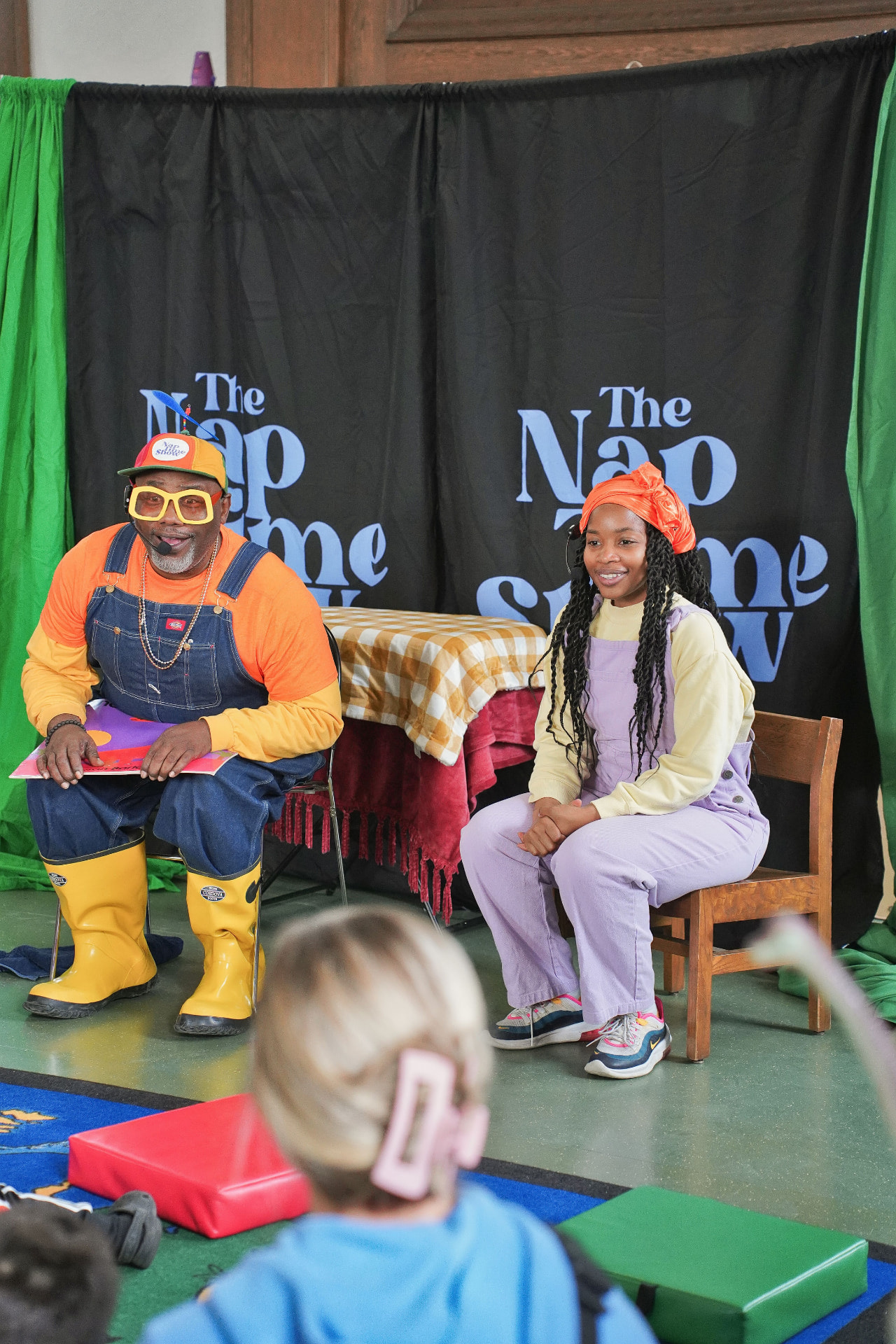 Mr. Nap Time and a co-host mid-story during a live show, seated in front of The Nap Time Show backdrop